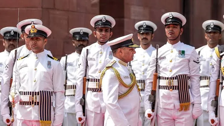 A senior naval officer in ceremonial dress inspects a guard of honour of sailors in white uniforms