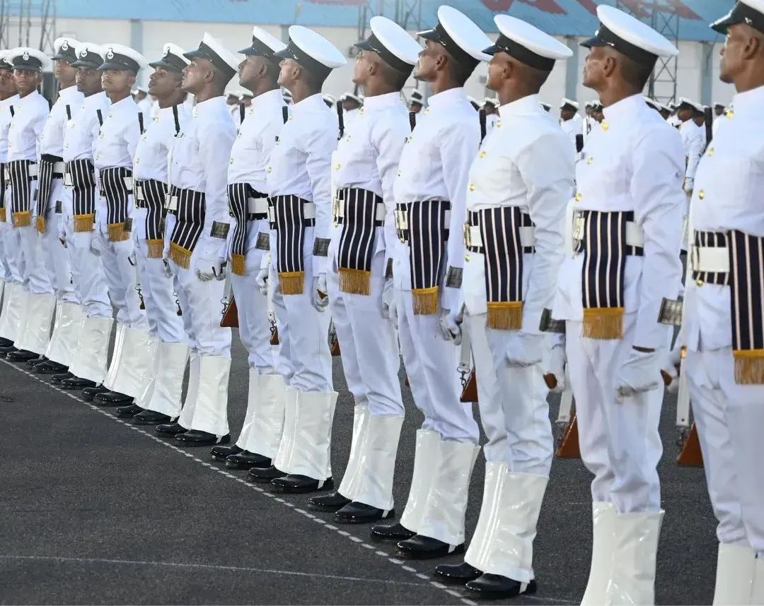A long line of sailors in ceremonial white uniforms standing at attention on a parade ground