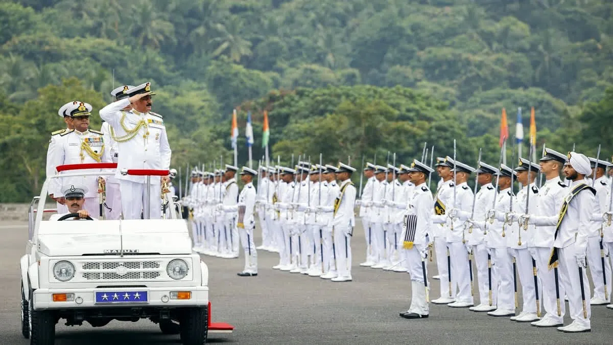 Officer cadets in white uniforms at a passing-out parade at a naval academy set against forested hills