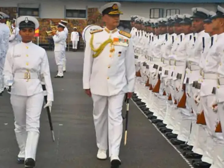 A naval officer in ceremonial whites inspects a line of sailors while a female officer cadet leads the parade