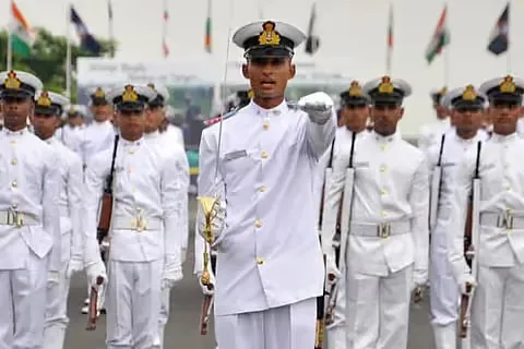 A naval cadet officer in white uniform leads ranks of cadets carrying ceremonial rifles at a passing-out parade